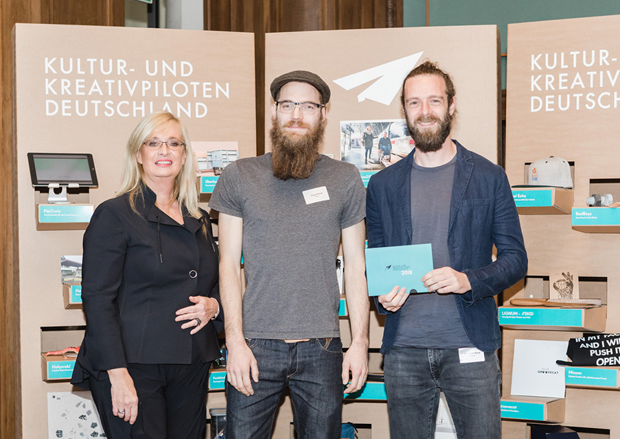 Preisverleihung der Kultur- und Kreativpiloten Deutschland 2018, drei Personen vor der Ausstellungswand